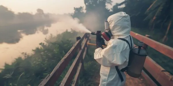 Health worker in a protective suit applying mosquito control fogging treatment
