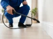 Technician applying home pest control spray along a baseboard