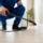 Technician applying home pest control spray along a baseboard