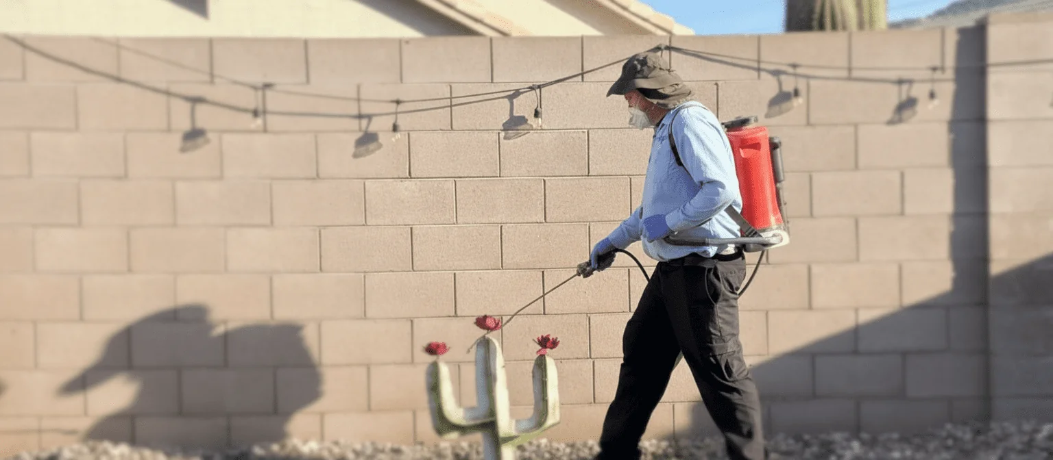 Technician applying home pest control spray along an outdoor backyard wall